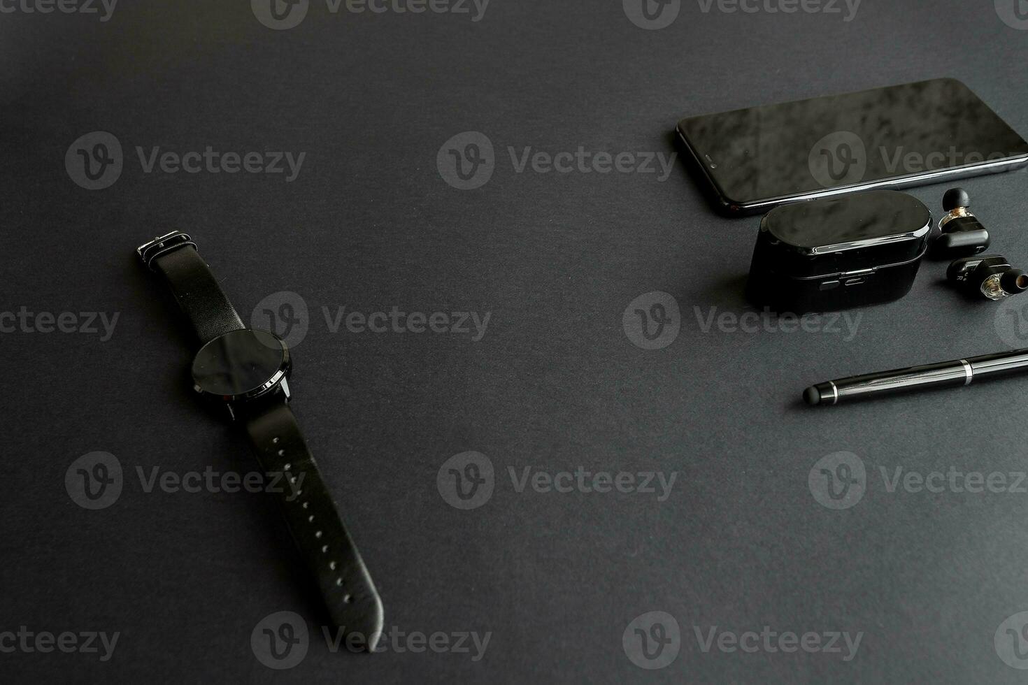 black pen, black smart watch, smartphone, wireless headphones on dark background photo