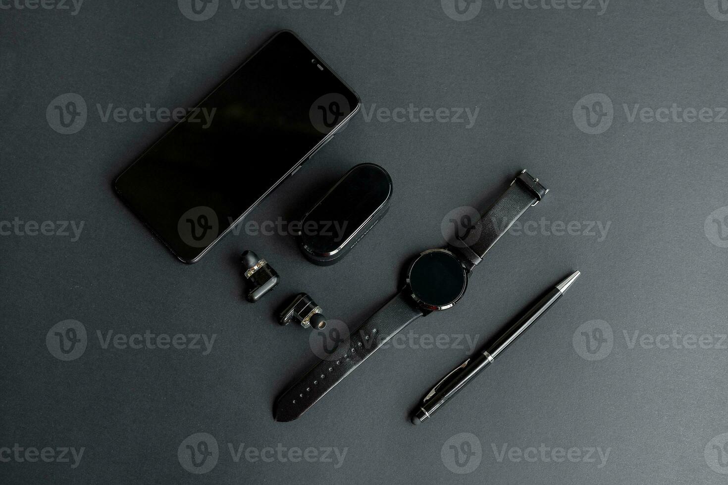 black pen, black smart watch, smartphone, wireless headphones on dark background photo