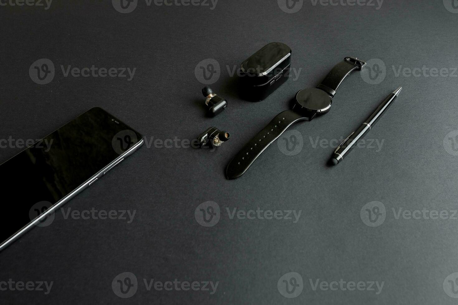 black pen, black smart watch, smartphone, wireless headphones on dark background photo