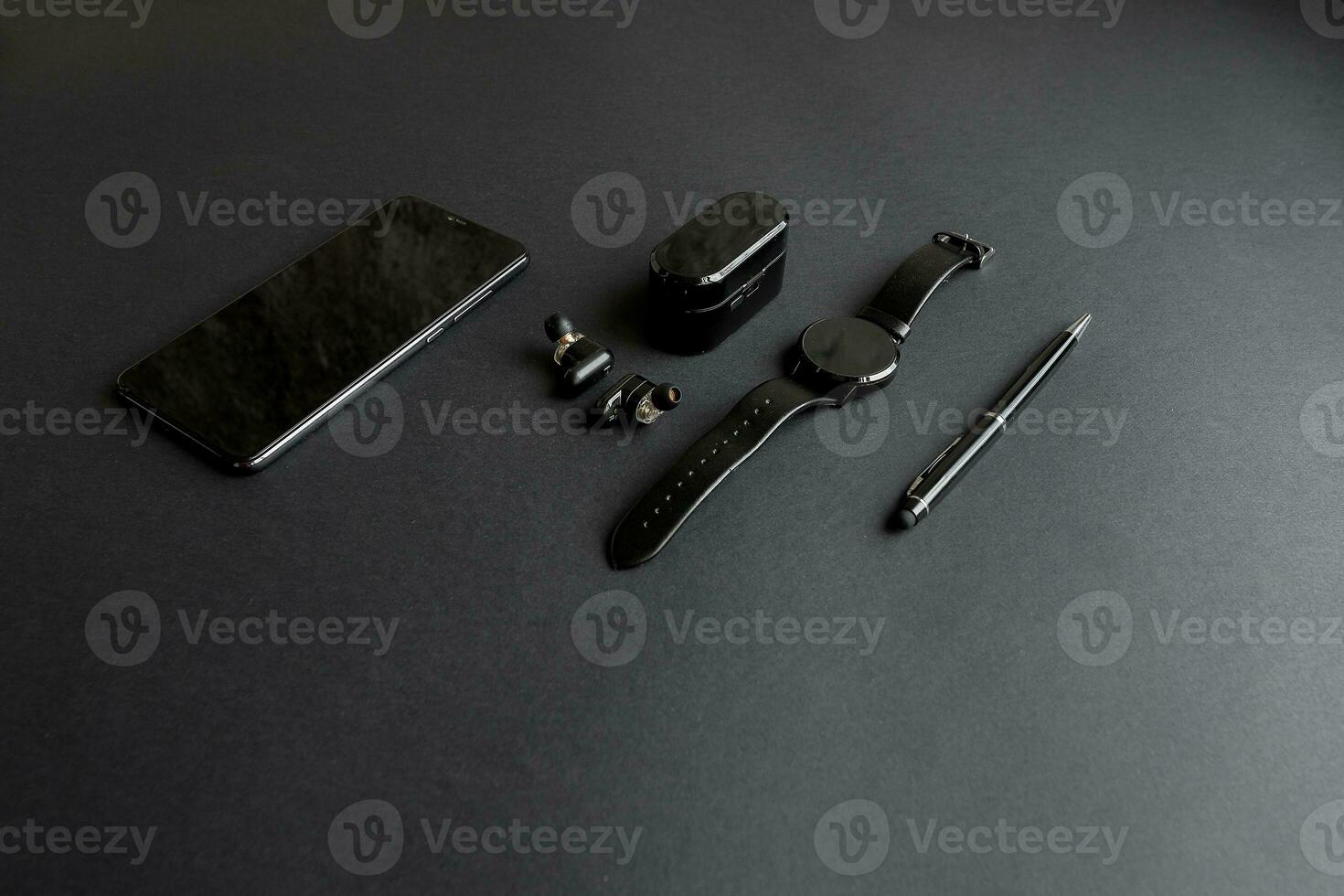 black pen, black smart watch, smartphone, wireless headphones on dark background photo