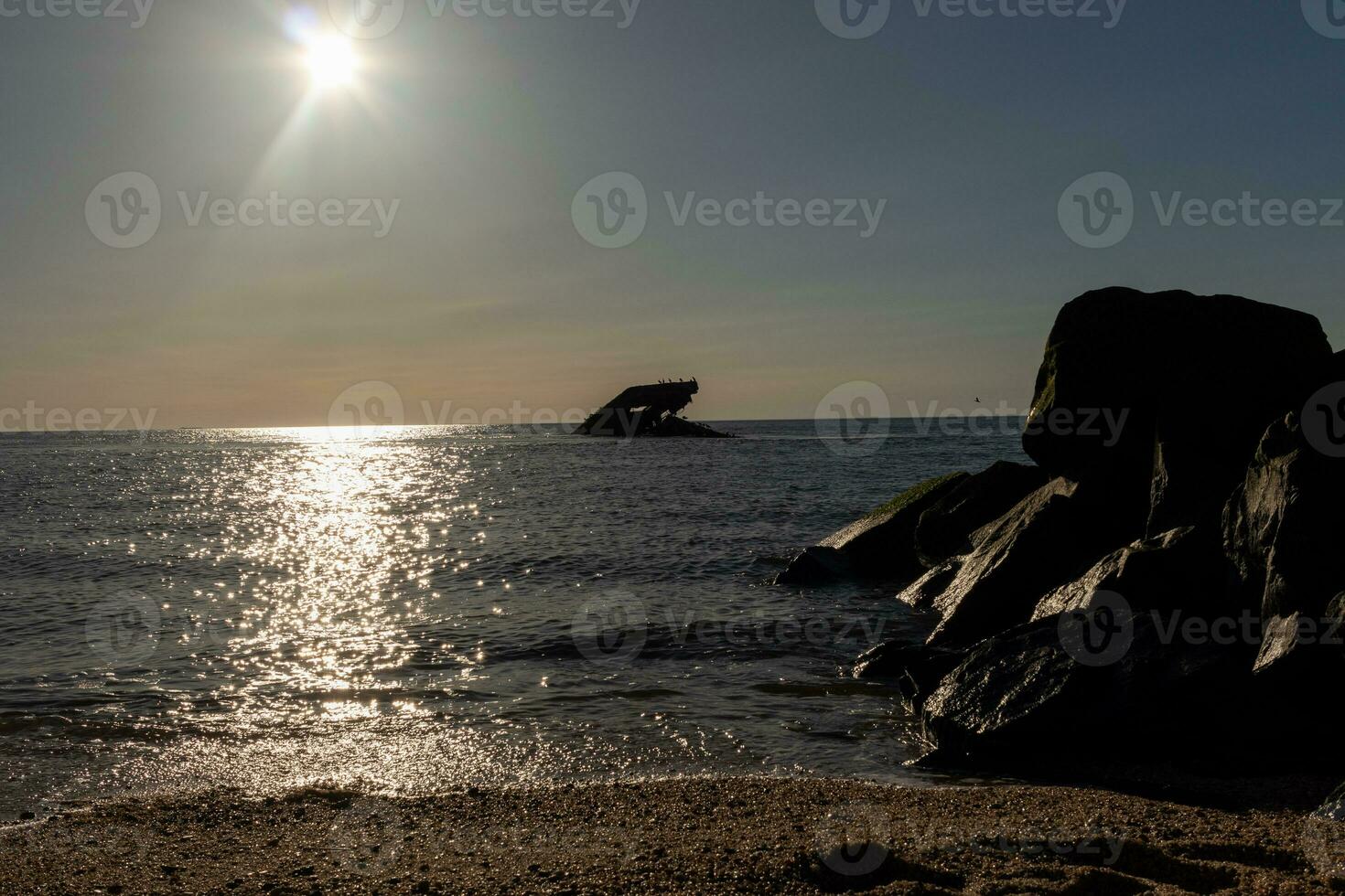 Sunset beach in Cape May New Jersey where you can get a great view of the sun going down across the ocean and the bay. The reflection of the sun on the water with the sunken ship looks so beautiful. photo