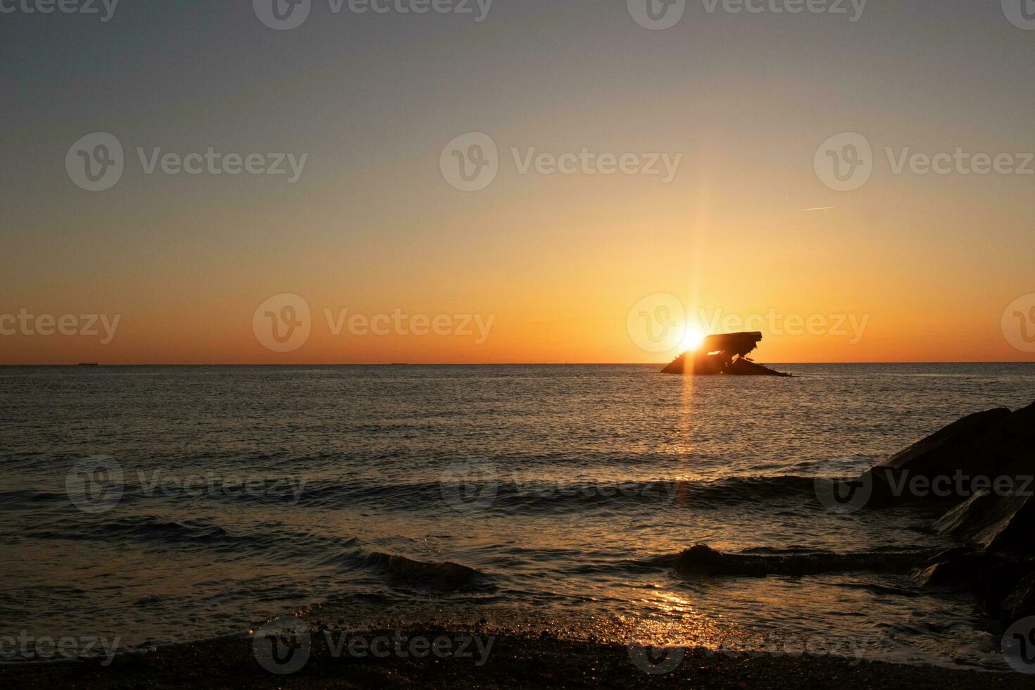 Sunset beach in Cape May New Jersey where you can get a great view of the sun going down across the ocean and the bay. The reflection of the sun on the water with the sunken ship looks so beautiful. photo