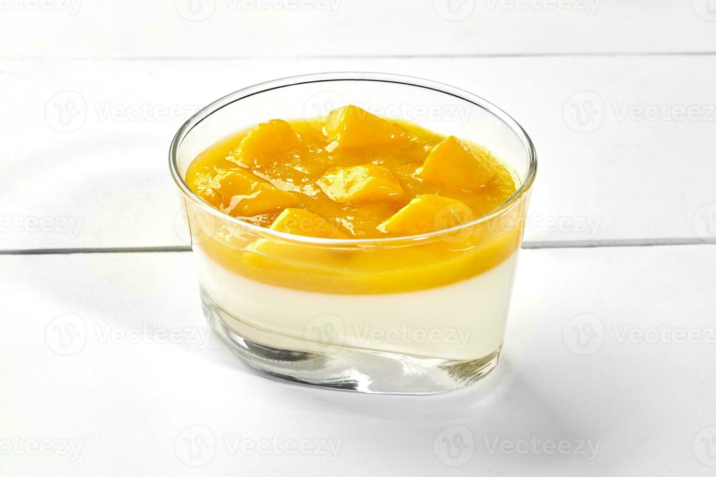 Vanilla panna cotta with mango puree in glass on white wooden background photo