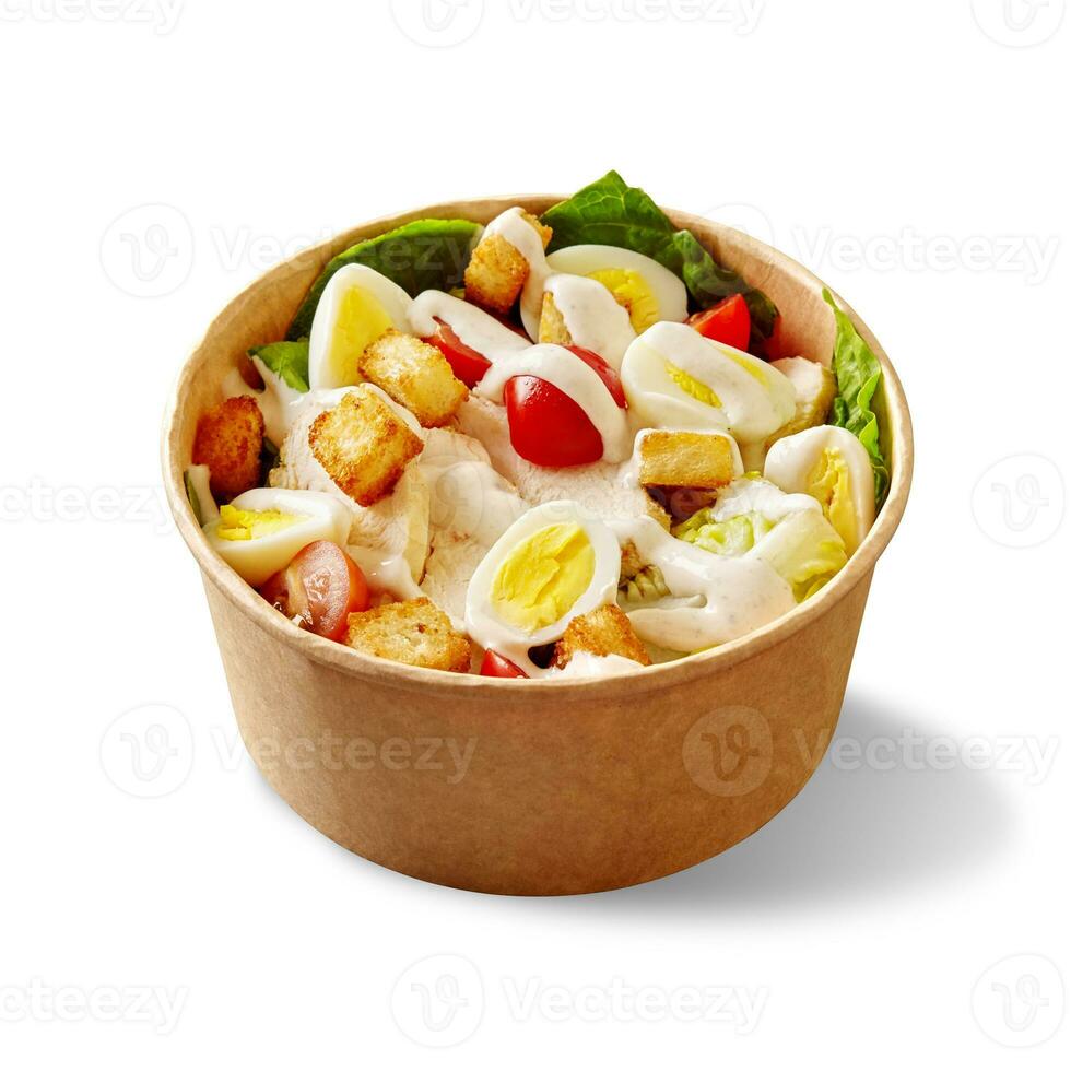 Caesar salad with lettuce, cherry tomatoes, quail eggs, croutons, chicken and sauce in cardboard bowl on white photo