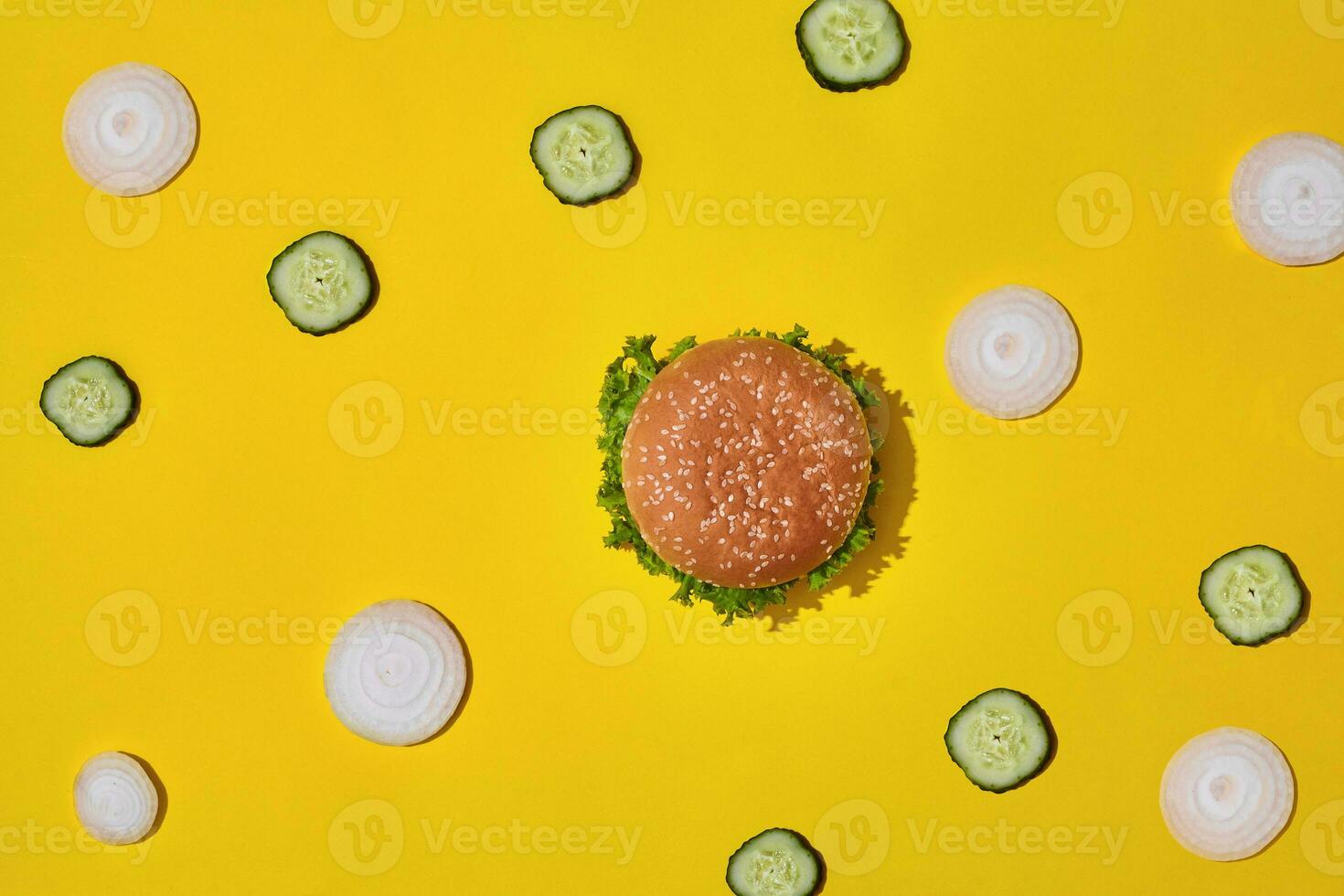Tasty fresh unhealthy hamburger with ketchup and vegetables on yellow vibrant bright background. Top View with Copy Space. photo