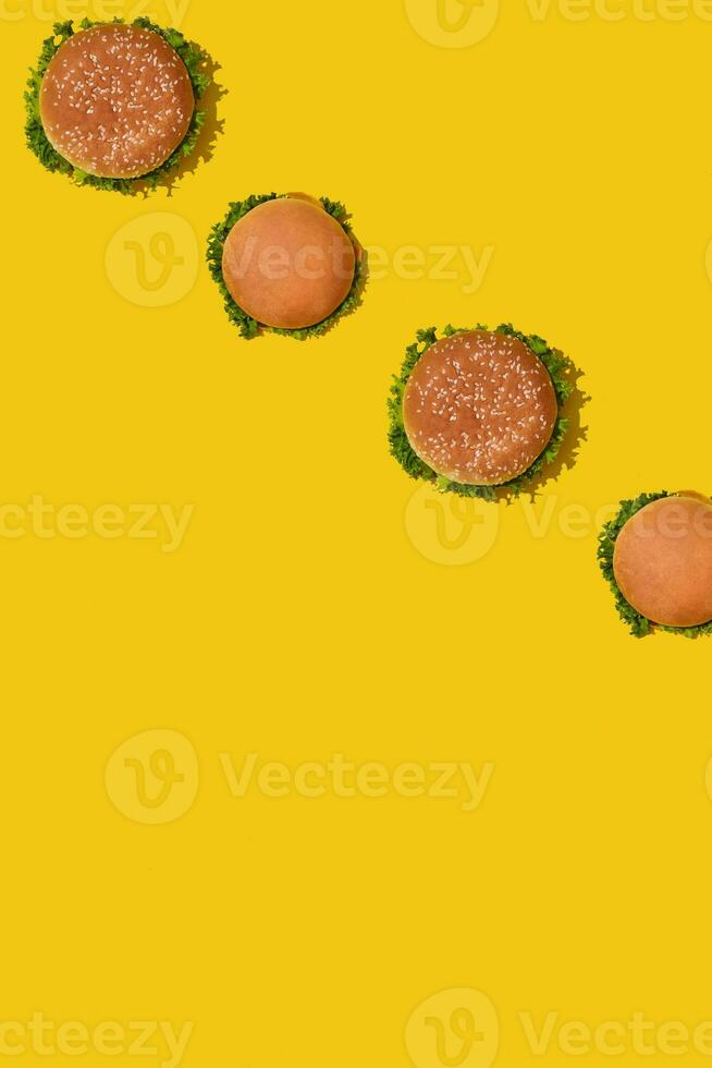 Many tasty fresh unhealthy hamburgers with ketchup and vegetables on yellow vibrant bright background. Top View with Copy Space. photo