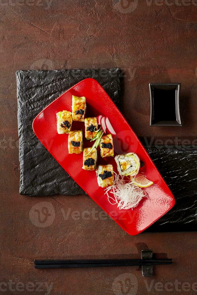 Uramaki rolls with avocado, shrimp, black tobiko, cream cheese, mango served with grated daikon on red plate photo