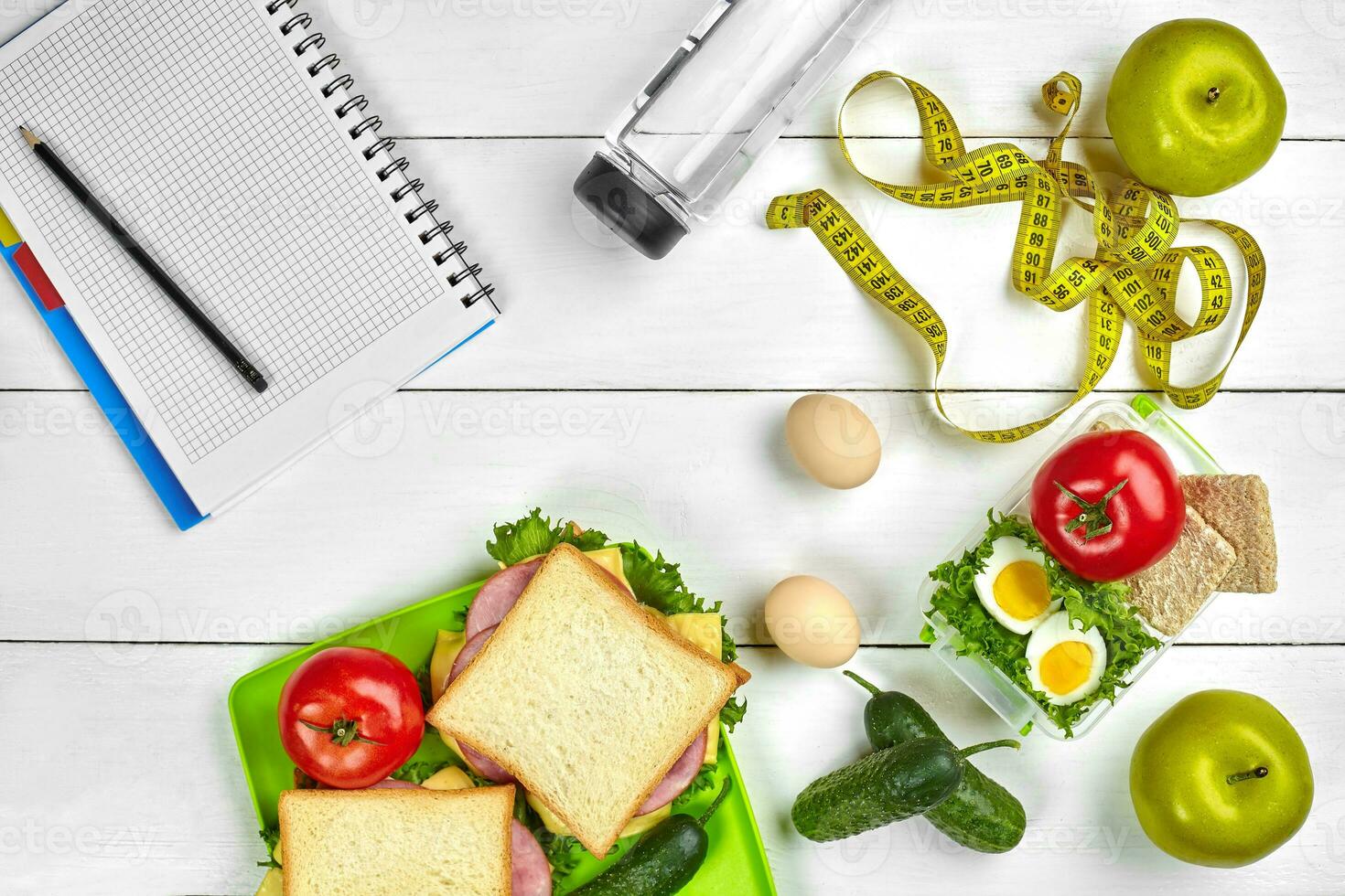 Healthy lunch in office at workplace or home. Whole-grain sandwich with ham and fresh vegetables and bottle of water. Top view, flat lay on wood photo