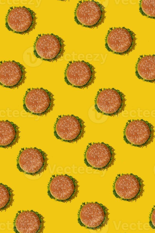 Many tasty fresh unhealthy hamburgers with ketchup and vegetables on yellow vibrant bright background. Top View with Copy Space. photo