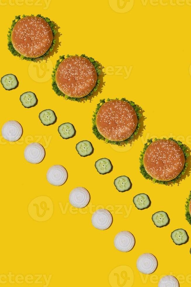 Many tasty fresh unhealthy hamburgers with ketchup and vegetables on yellow vibrant bright background. Top View with Copy Space. photo