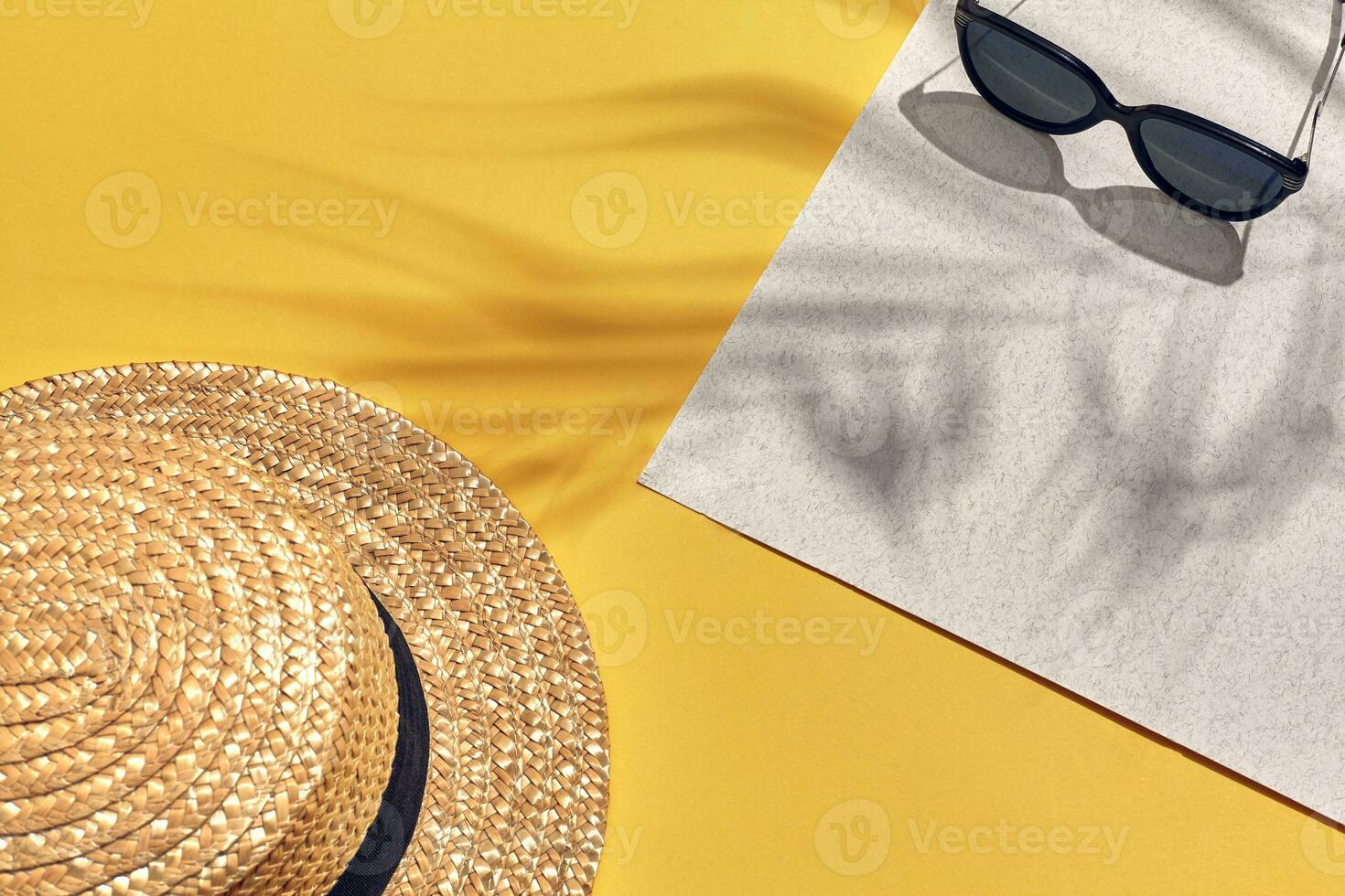 Straw beach woman's hat and sun glasses, top view yellow and white paper background with shadow from a palm leaf. photo
