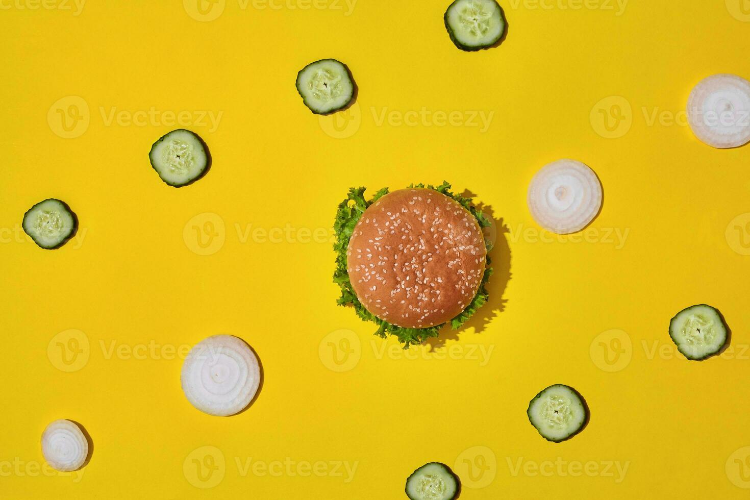 Tasty fresh unhealthy hamburger with ketchup and vegetables on yellow vibrant bright background. Top View with Copy Space. photo