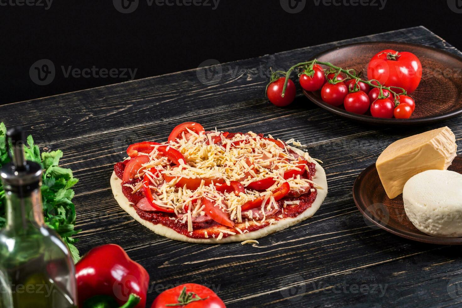 Raw dough for pizza preparation with ingredient tomato sauce, mozzarella, tomatoes, basil, olive oil, cheese, spices served on rustic wooden table. photo