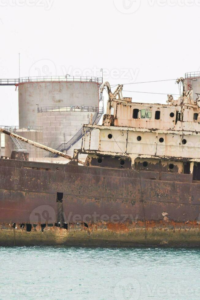 an old ship in the water near a refinery photo