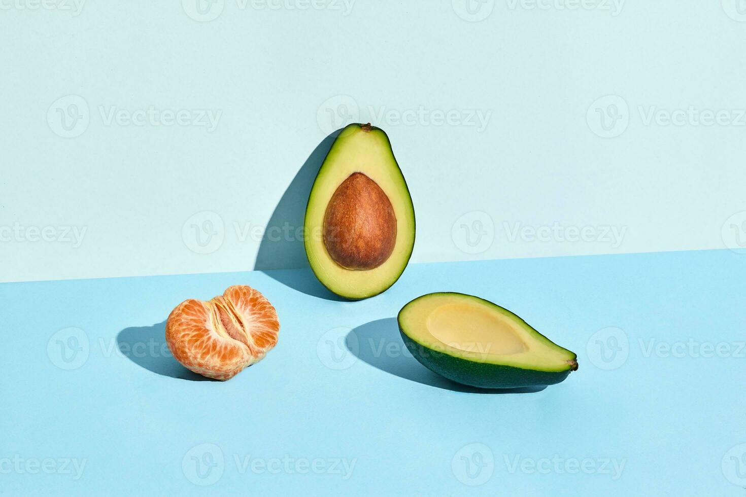 Composition of fresh fruits, mandarin and two halfs of cutted avocado on two-colored background photo
