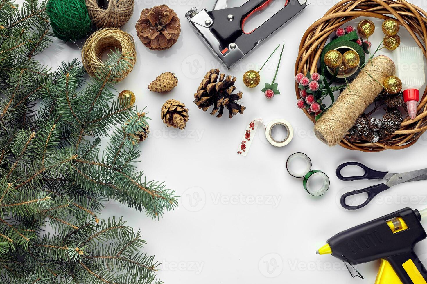 Preparing for Christmas or New Year holiday. Flat-lay of fur tree branches, wreaths, rope, scissors, craft paper over white table background, top view. photo