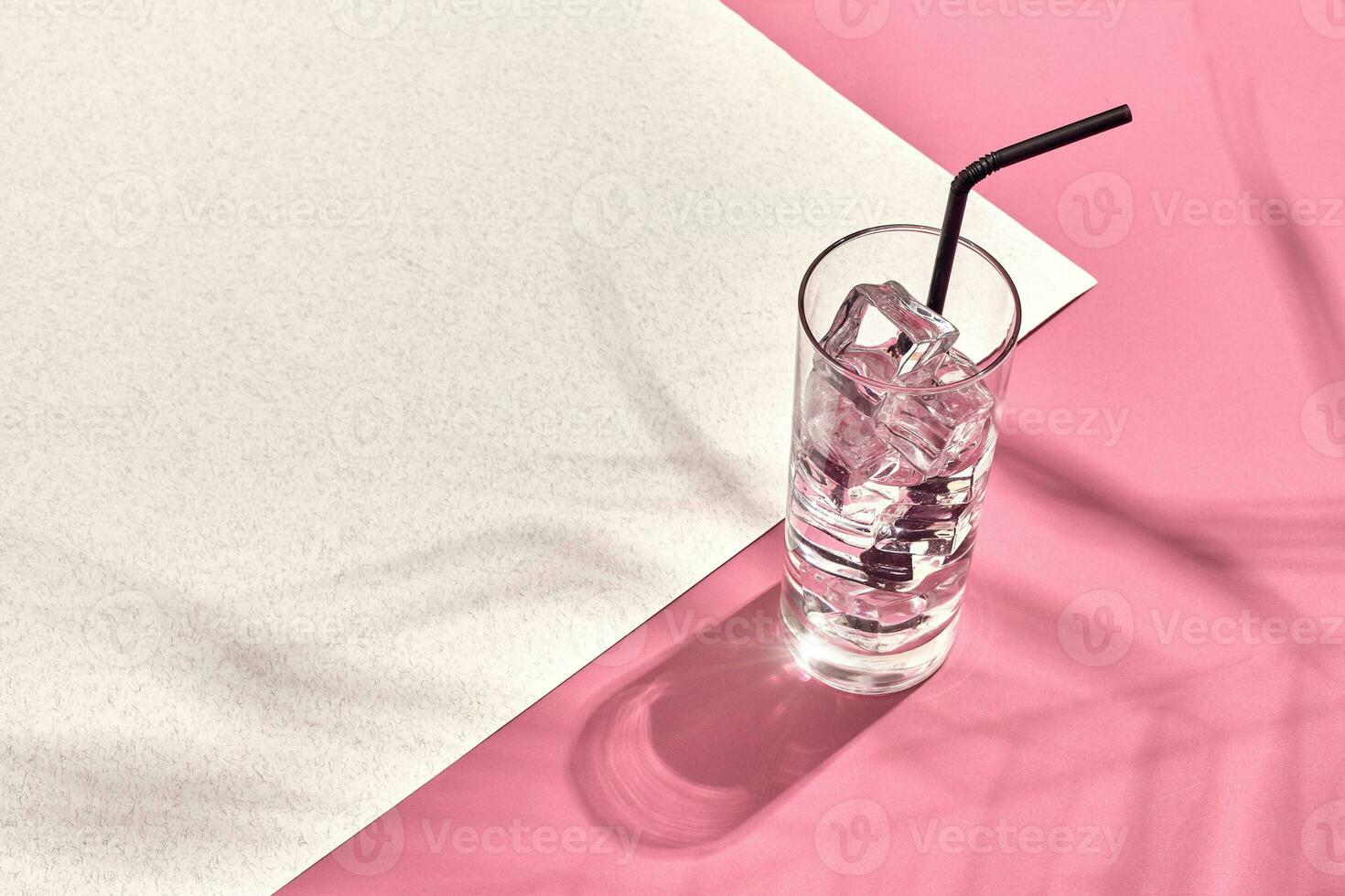 Glass of mineral water with ice on pink and white background with shadow from a palm leaf photo