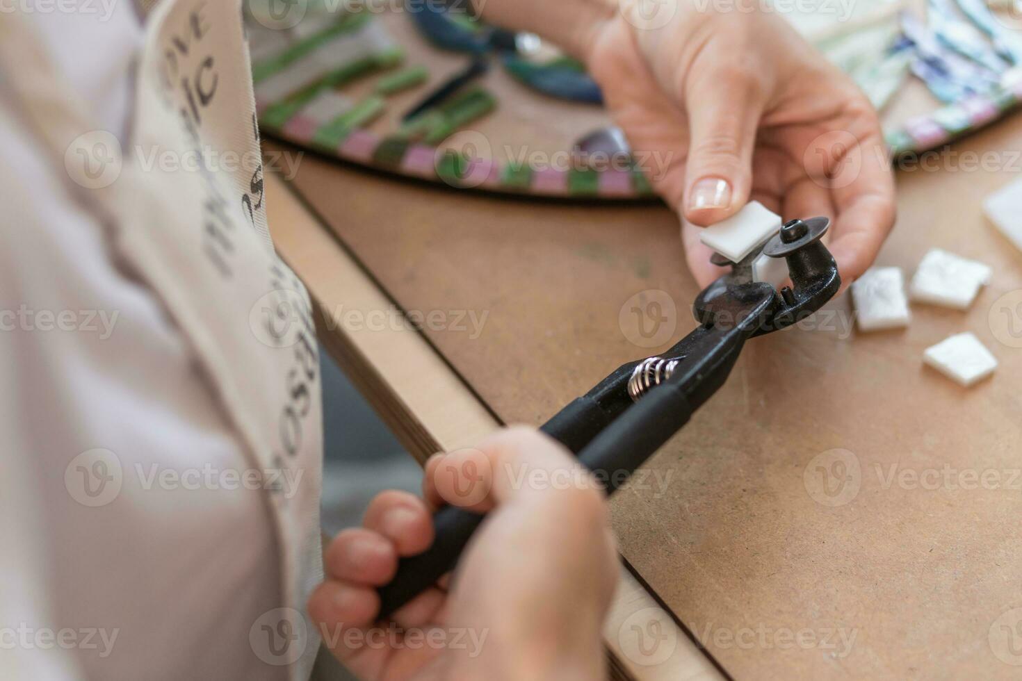 Workplace of the mosaic master women's hands holding tool for mosaic details in the process of making a mosaic photo