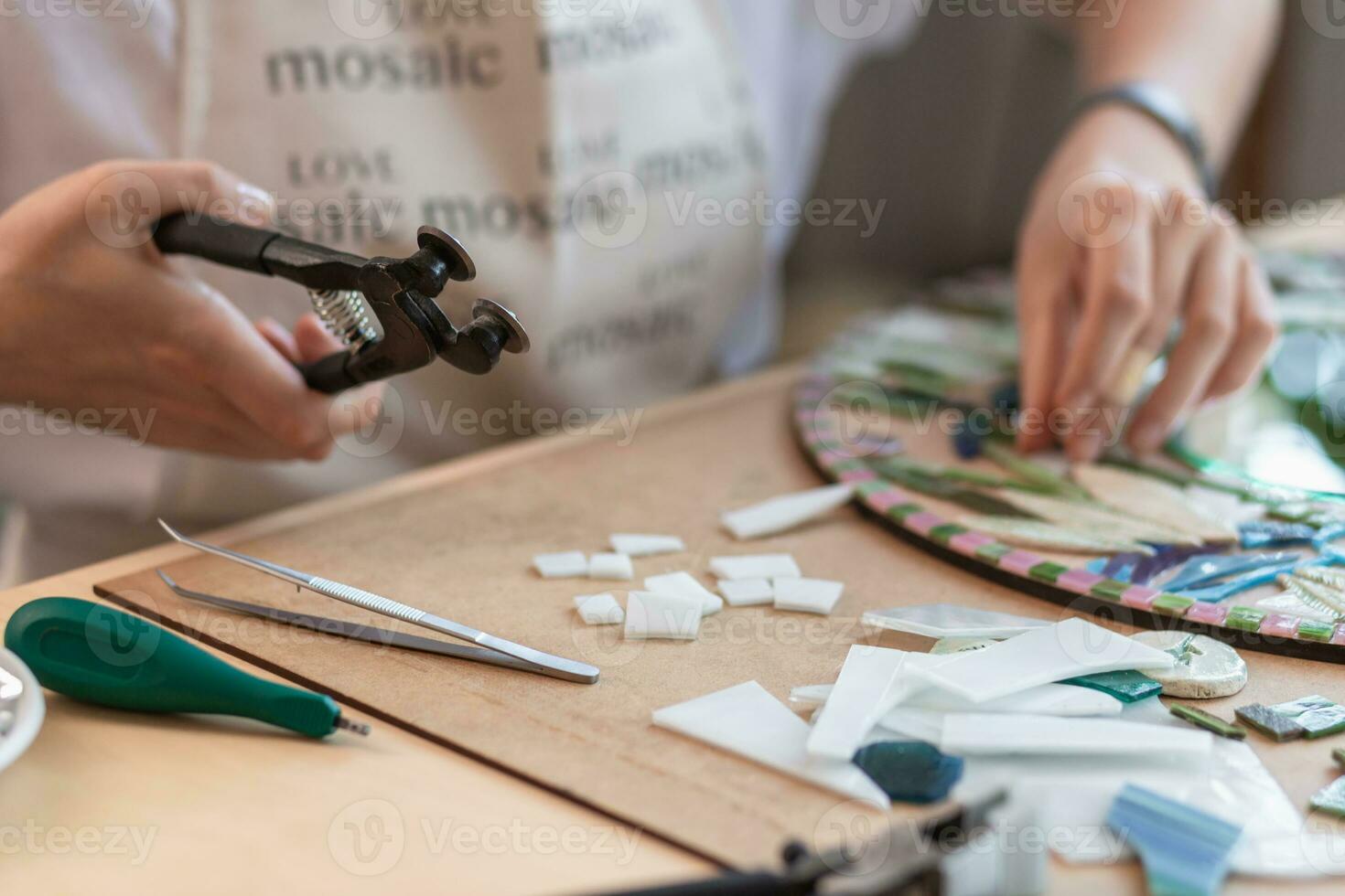 Workplace of the mosaic master women's hands holding tool for mosaic details in the process of making a mosaic photo