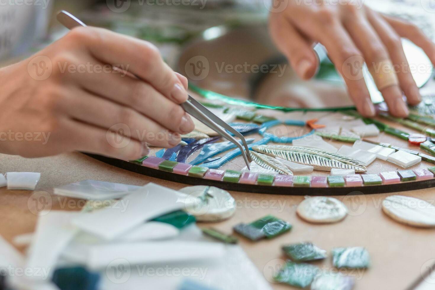 Workplace of the mosaic master women's hands holding tool for mosaic details in the process of making a mosaic photo