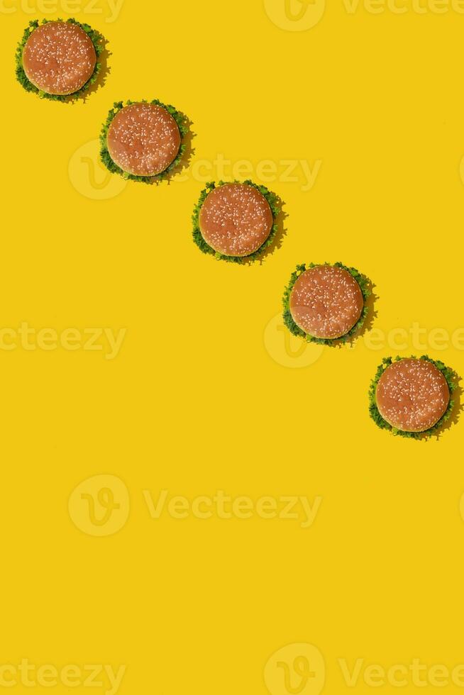 Many tasty fresh unhealthy hamburgers with ketchup and vegetables on yellow vibrant bright background. Top View with Copy Space. photo