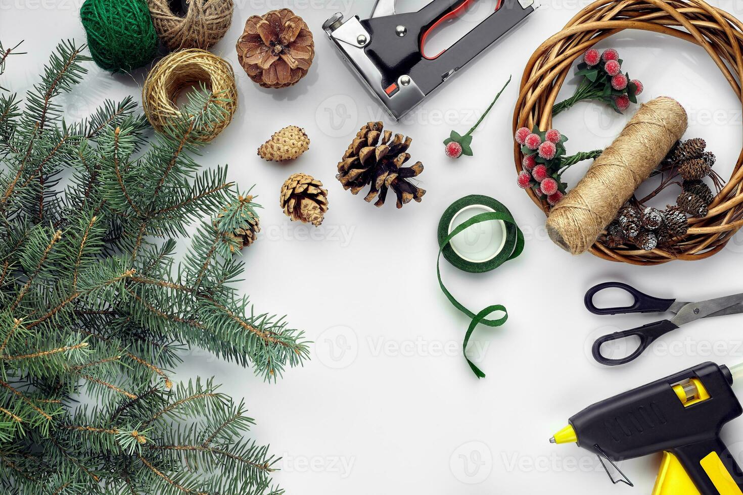 Preparing for Christmas or New Year holiday. Flat-lay of fur tree branches, wreaths, rope, scissors, craft paper over white table background, top view. photo