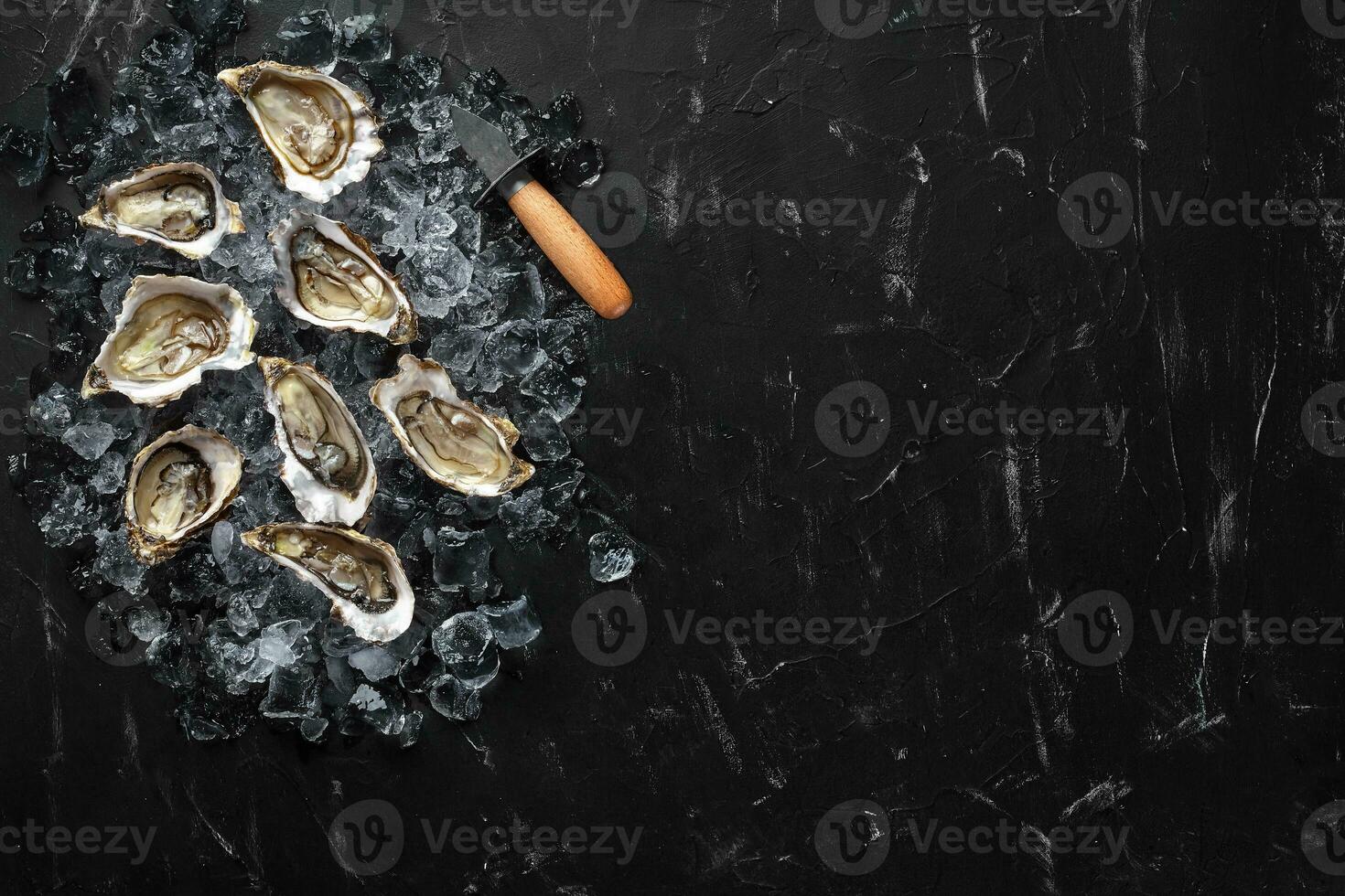 Fresh opened oysters and ice on a black stone textured background. Top view with copy space. Close-up shot. photo