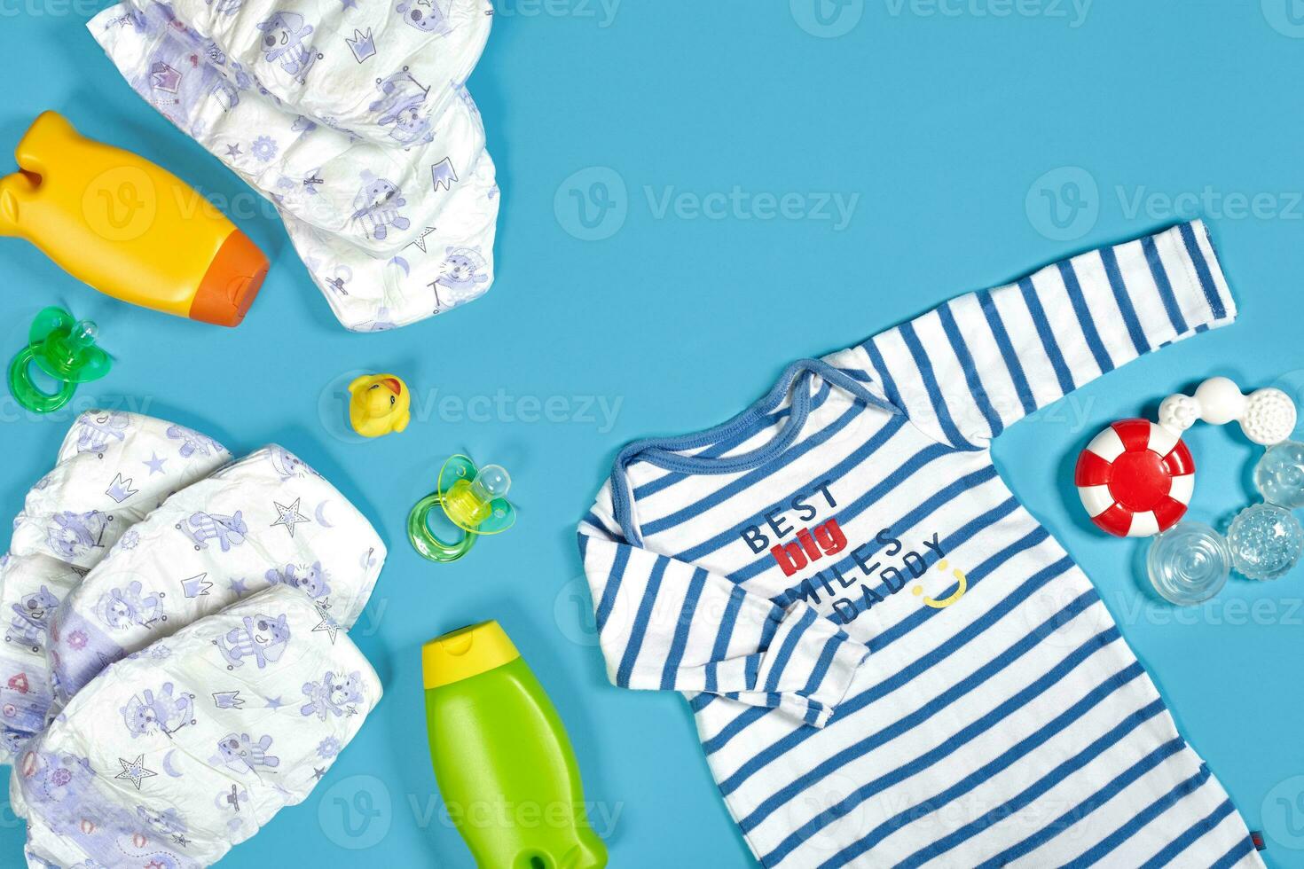 Baby care with bath set. Nipple, toy, clothes, shampoo on blue background top view mockup photo