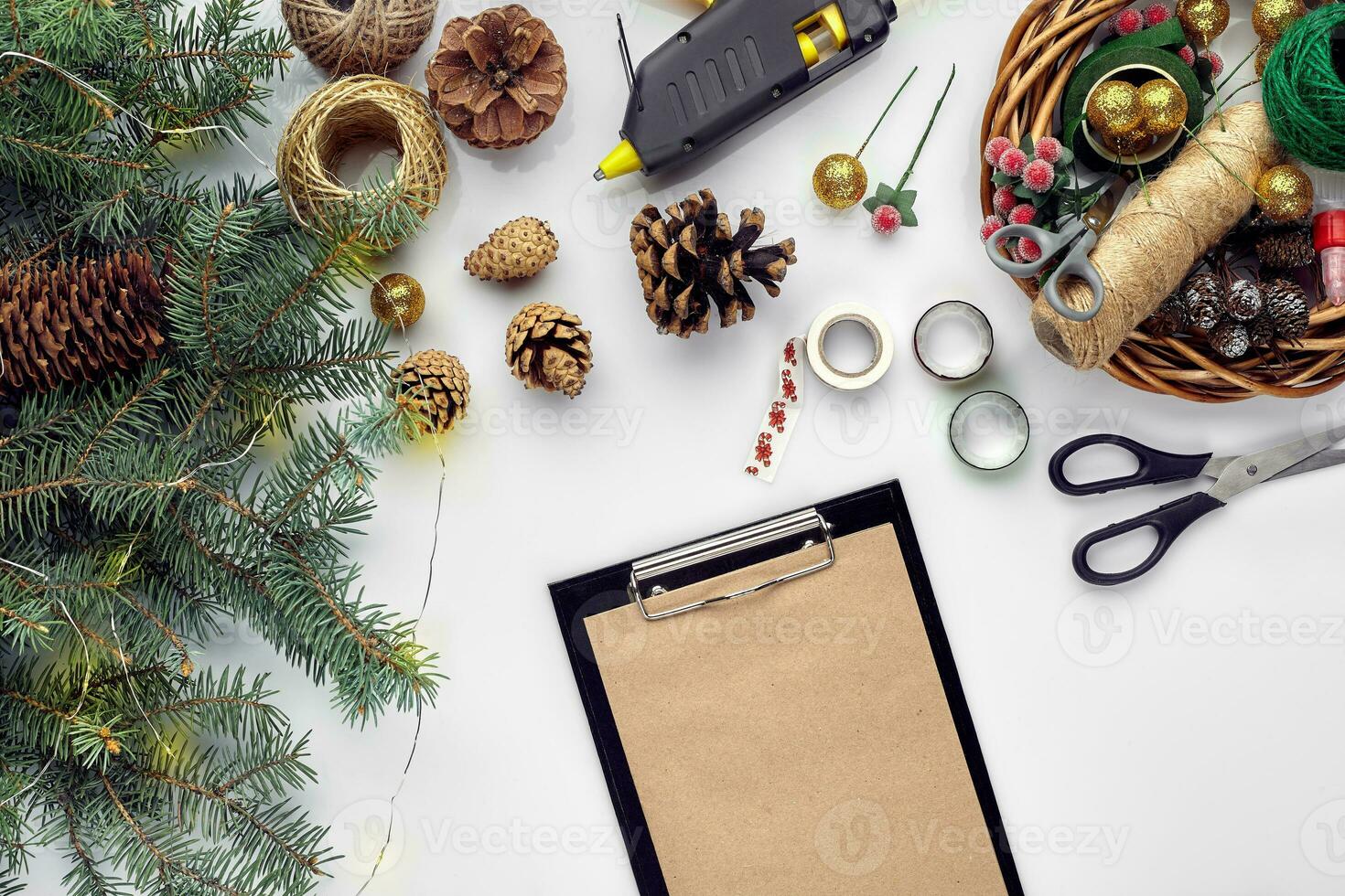 Preparing for Christmas or New Year holiday. Flat-lay of fur tree branches, wreaths, rope, scissors, craft paper over white table background, top view. photo