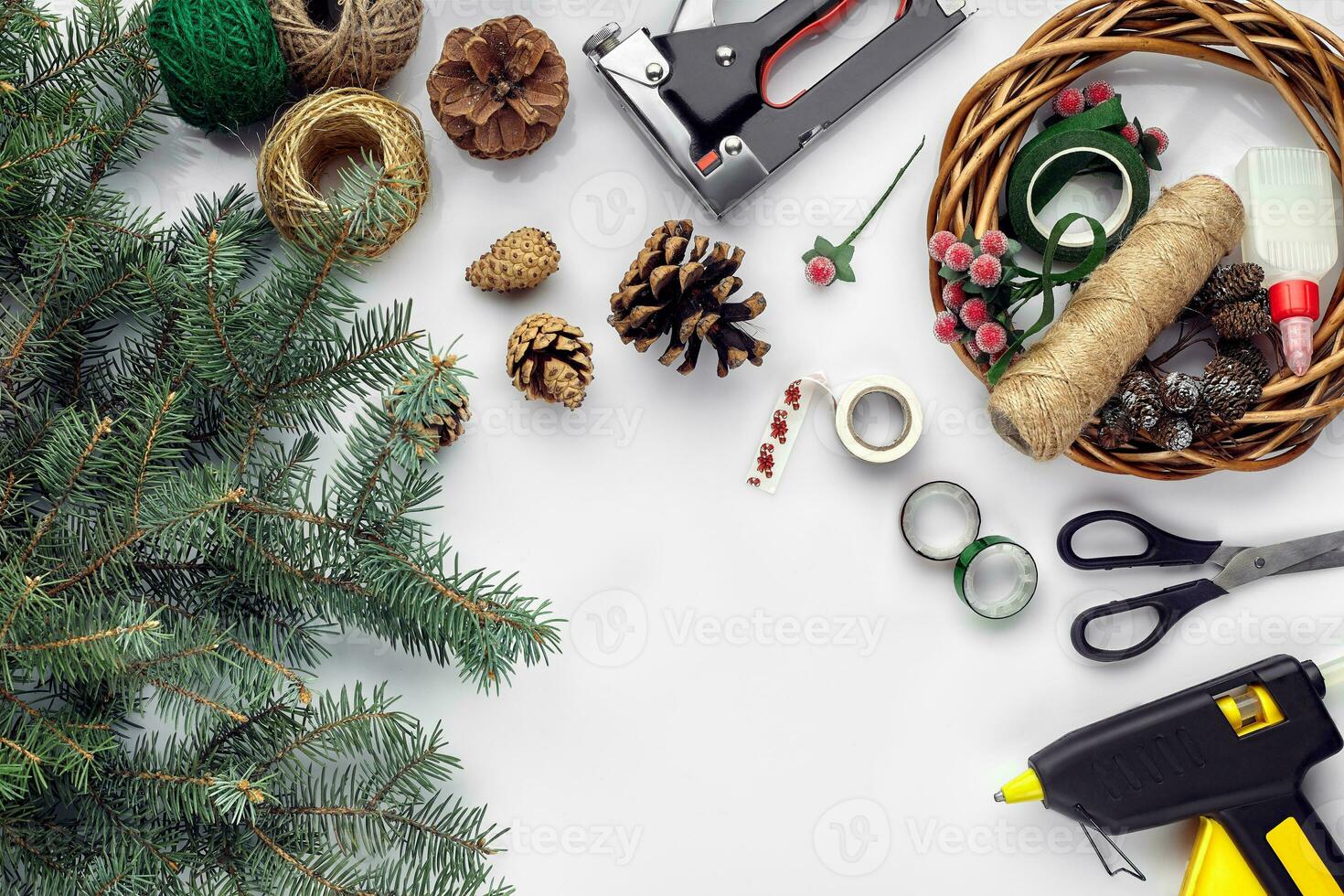 Preparing for Christmas or New Year holiday. Flat-lay of fur tree branches, wreaths, rope, scissors, craft paper over white table background, top view. photo