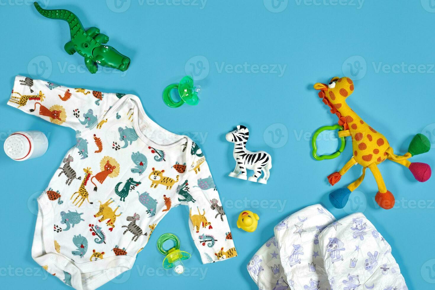 Babies goods cloth diaper, baby powder, nibbler, cream, teether, soother, baby toy on blue background. Copy space. Top view. photo