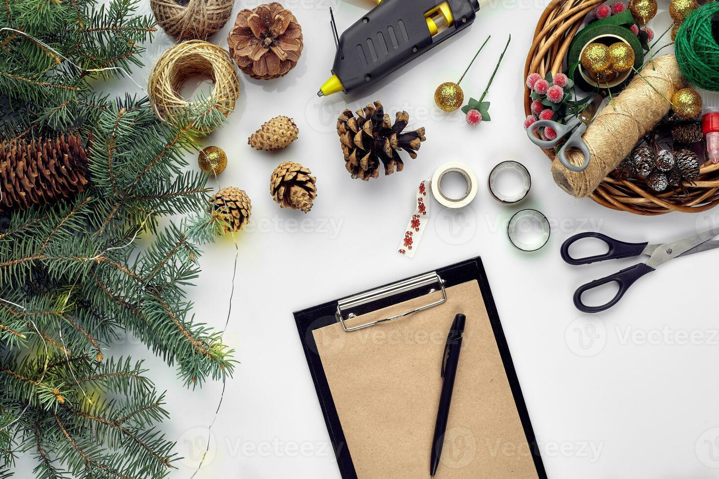 Preparing for Christmas or New Year holiday. Flat-lay of fur tree branches, wreaths, rope, scissors, craft paper over white table background, top view. photo