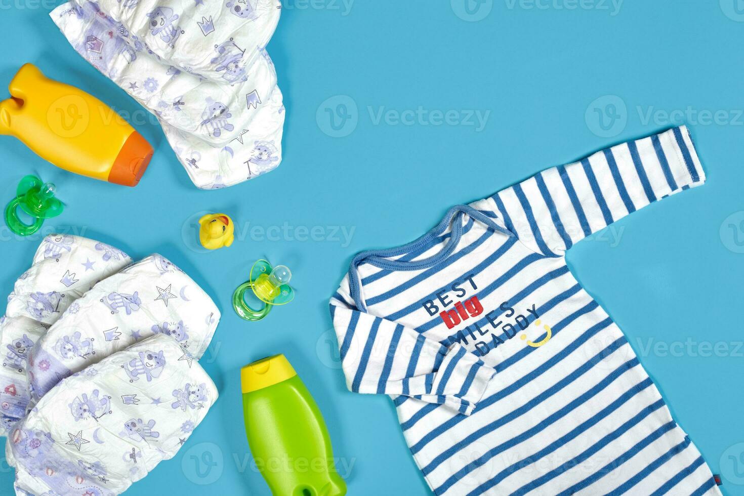 Baby care with bath set. Nipple, toy, clothes, shampoo on blue background top view mockup photo