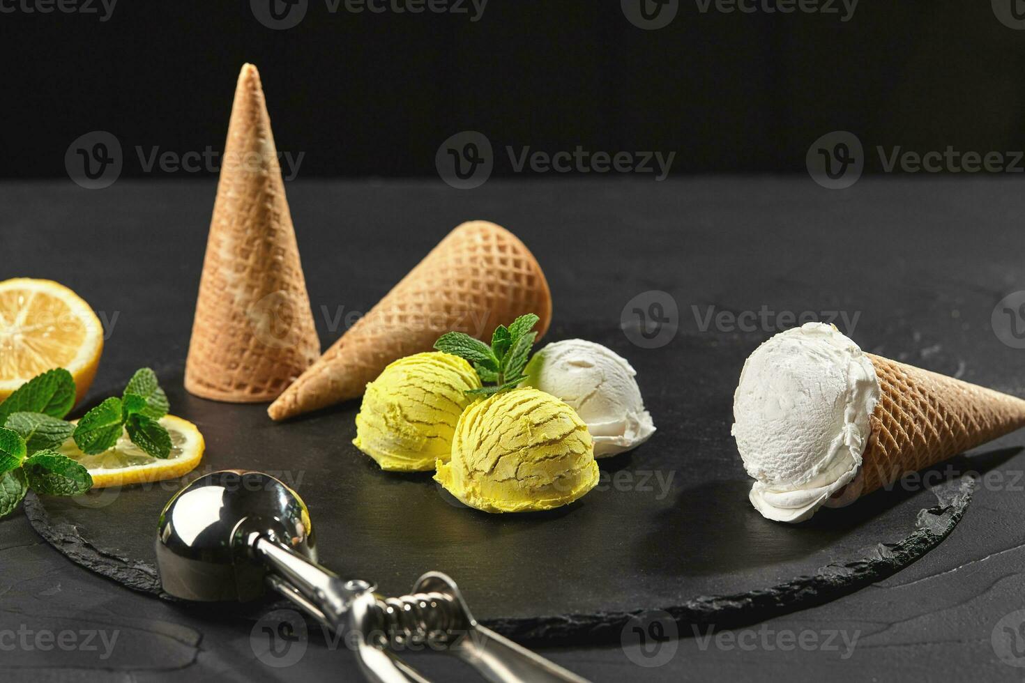 Tasty creamy and citrus lemon ice cream decorated with mint served on a stone slate over a black background. photo