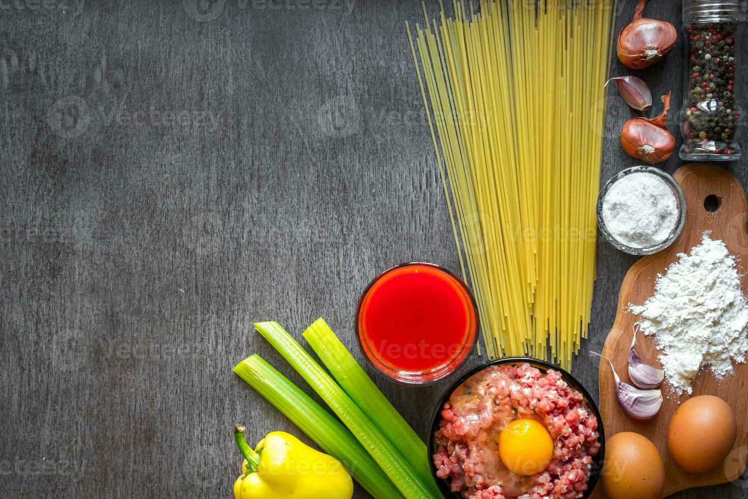 Ingredients for cooking pasta. Spaghetti, tomato juice, olive oil, garlic, minsed meat, pepper and fresh celery on wooden background, top view, copy space photo