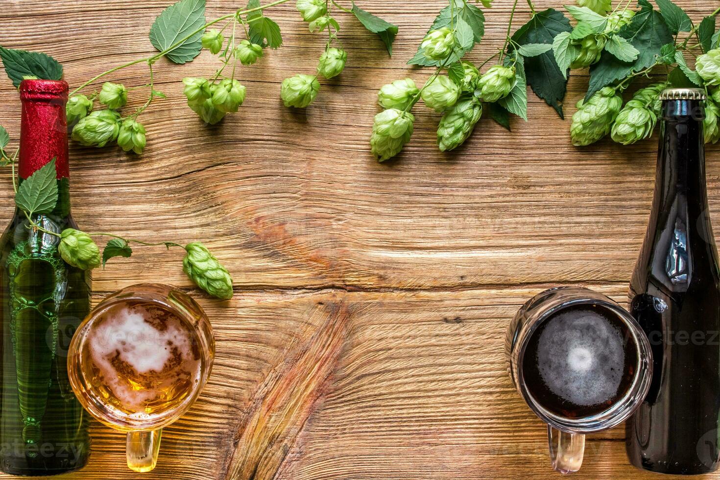 Bottle and a glass of light and dark beer with hops and copy space area on wooden background. Top view photo