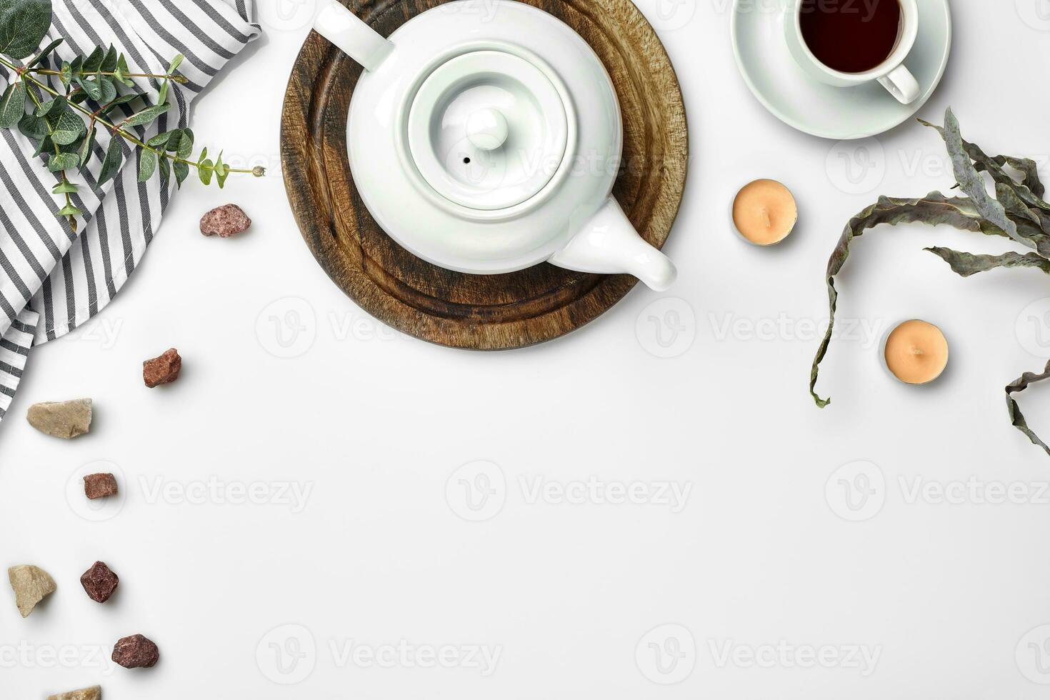 A white porcelain teapot on a wooden board and a white cup with tea on a table. Top view. Copy space. photo