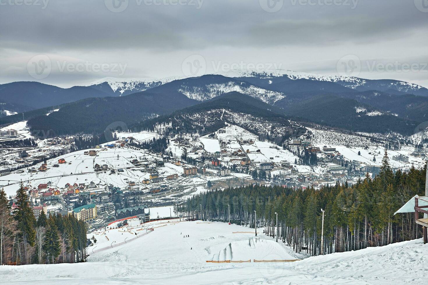 Panorama of ski resort, slope, people on the ski lift, skiers on the piste among green pine trees and snow lances. photo