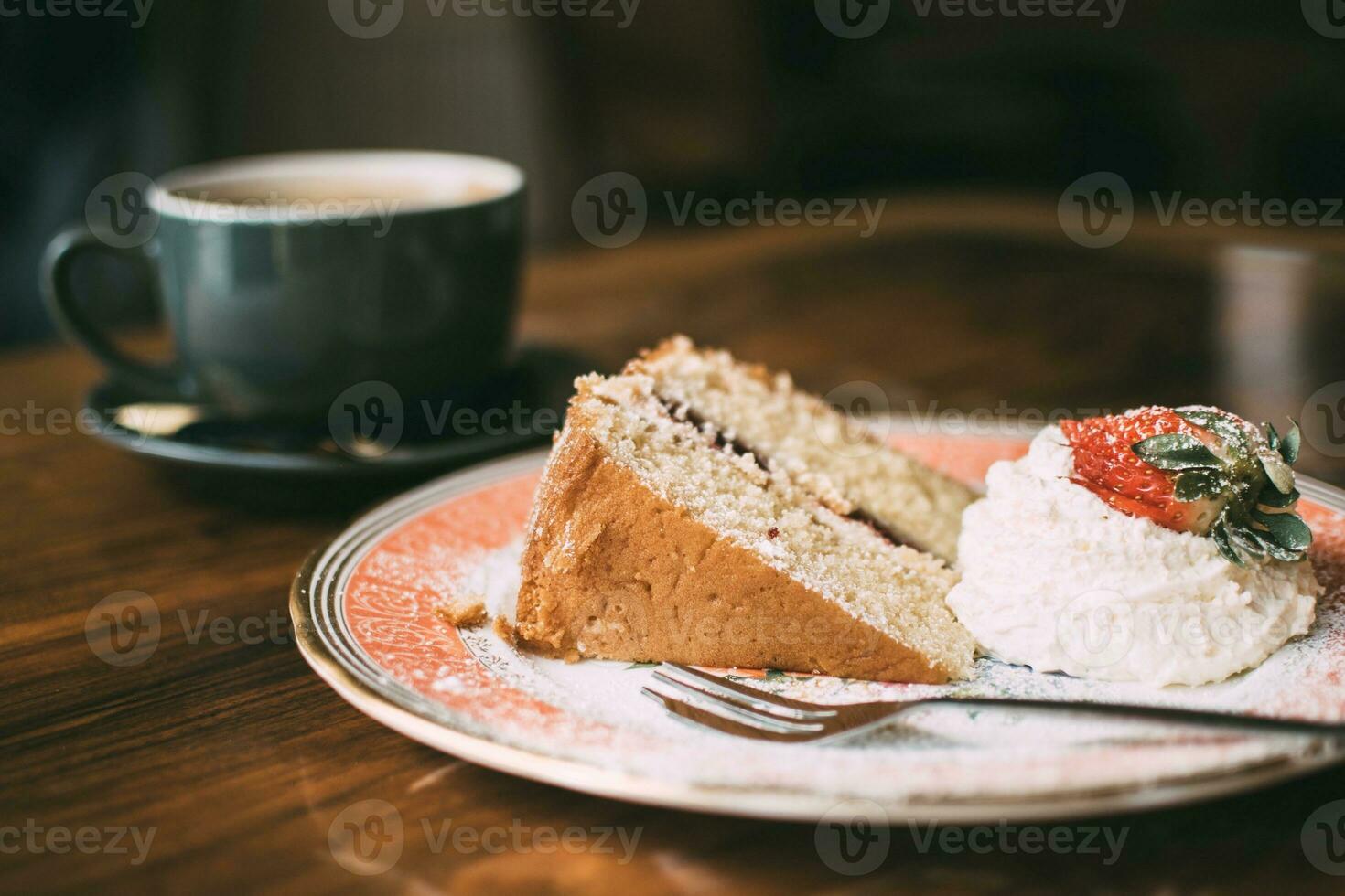 Piece of cake with strawberry and cup of coffee on the wooden table photo