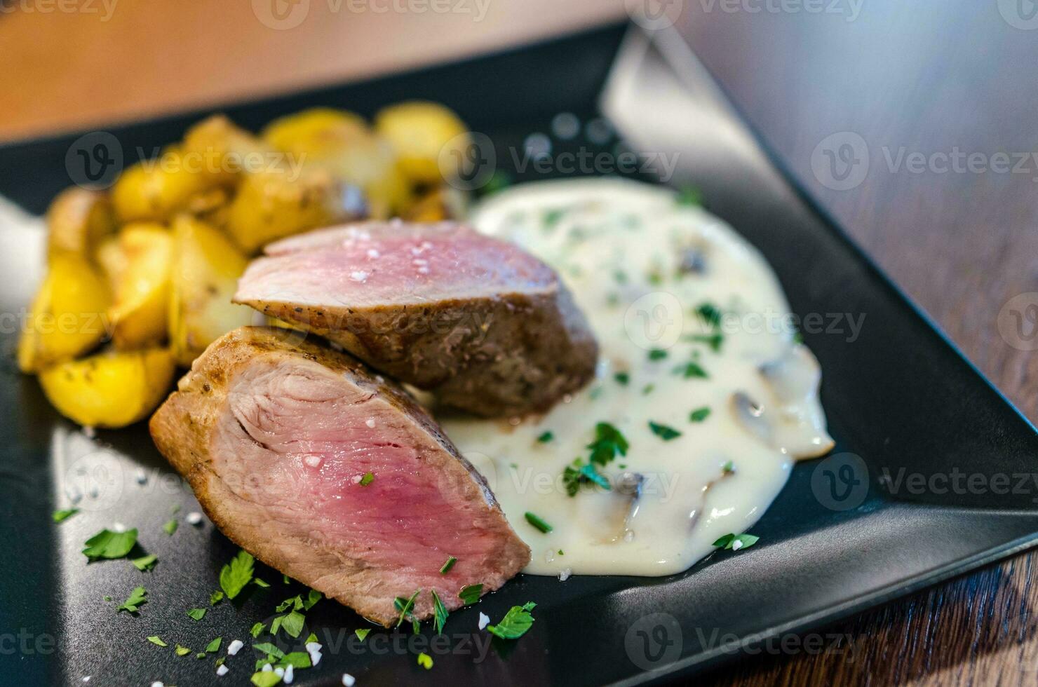 Roast duck breast with mashed potatoes and mushroom sauce on black plate photo