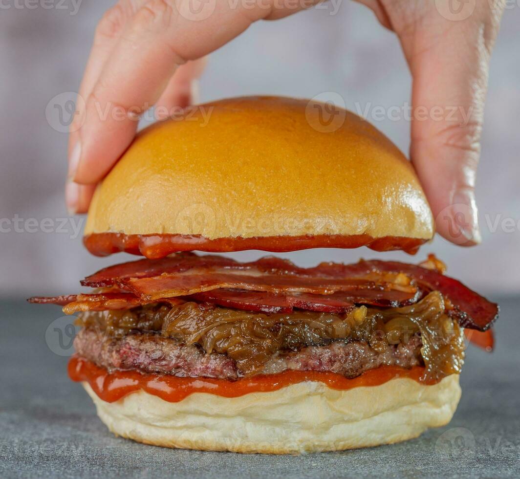 Close-up of woman's hand holding hamburger with bacon. photo