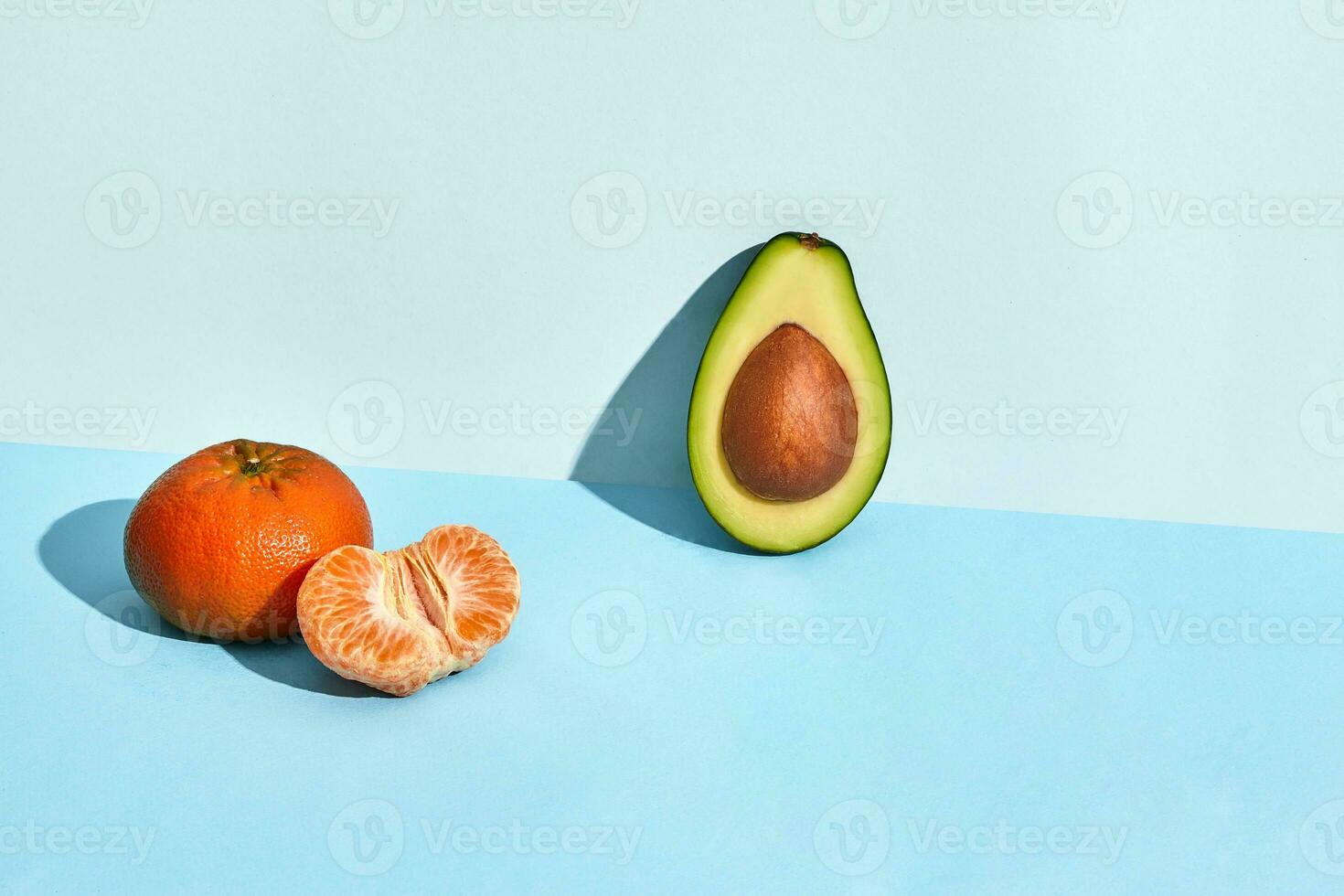 Composition of fresh fruits, mandarin and half of cutted avocado on two-colored background photo