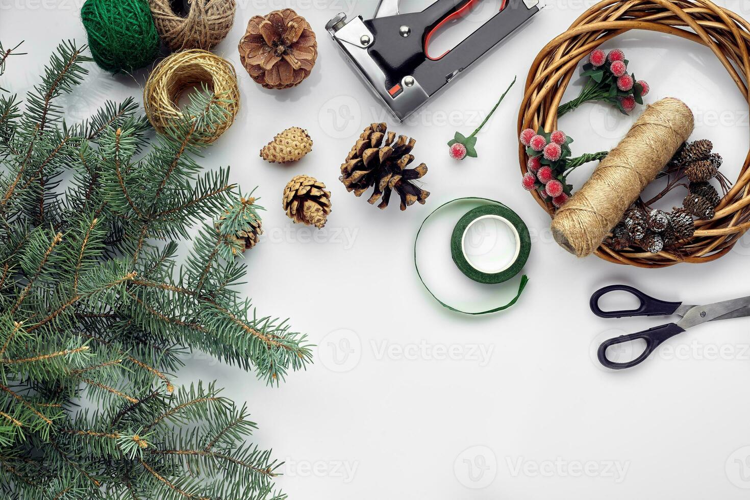 Preparing for Christmas or New Year holiday. Flat-lay of fur tree branches, wreaths, rope, scissors, craft paper over white table background, top view. photo