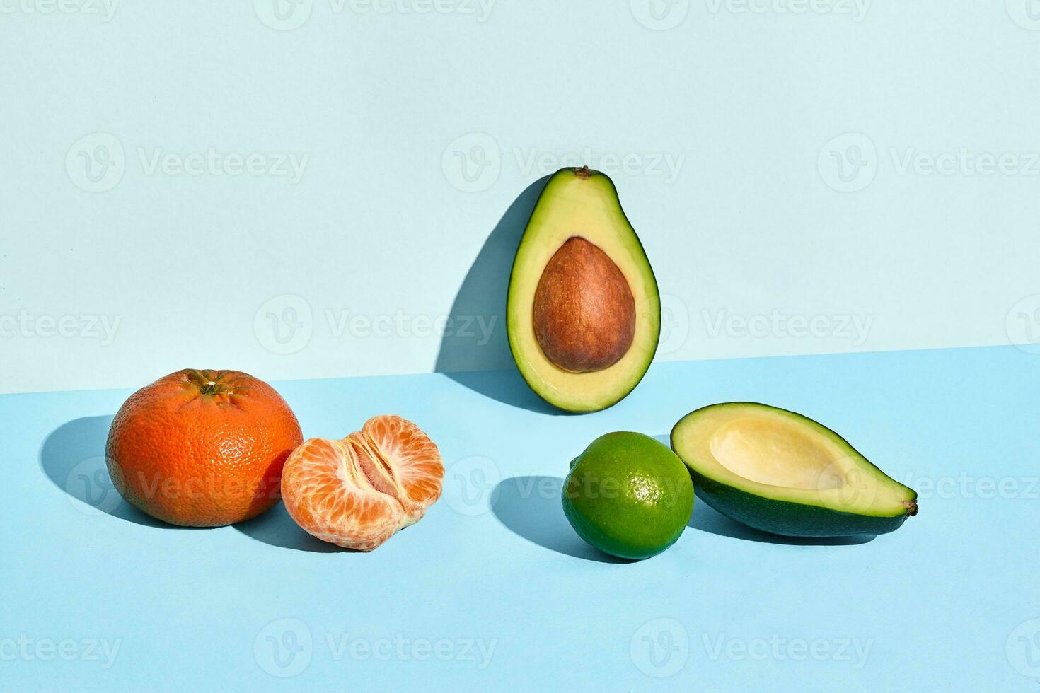 Composition of fresh fruits, mandarin lime and two halfs of cutted avocado on two-colored background photo