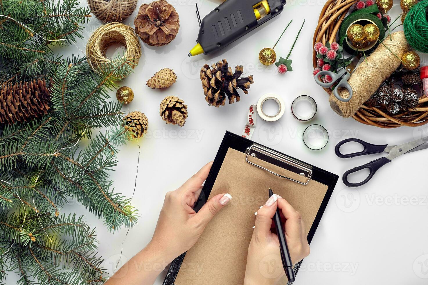 Preparing for Christmas or New Year holiday. Flat-lay of fur tree branches, wreaths, rope, scissors, craft paper over white table background, top view. photo