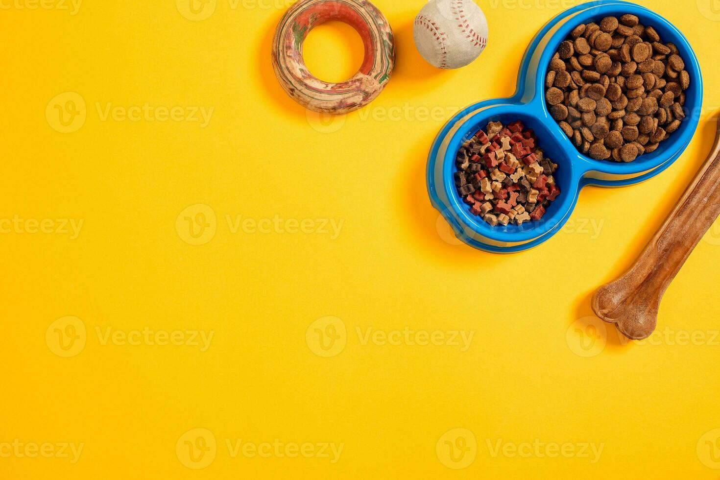 Dry pet food in bowl with a ball and dog bone on yellow background top view photo