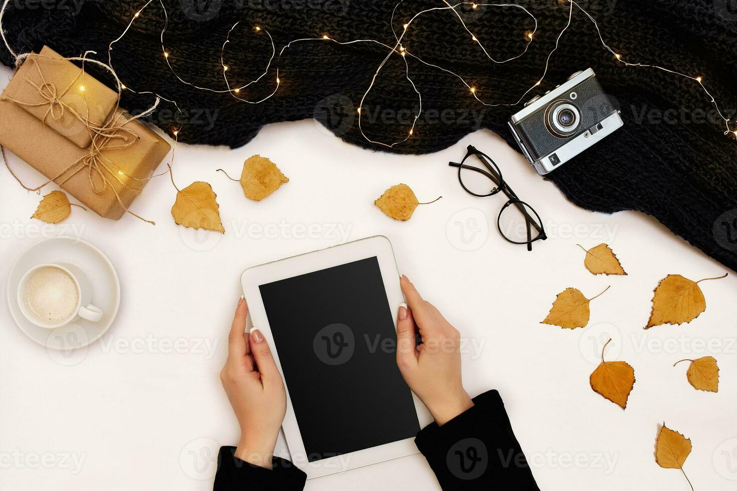 Top view,close-up of tablet computer with blank screen in hands of woman dressed in knitted sweater. Nearby is cup of coffee and scarf photo