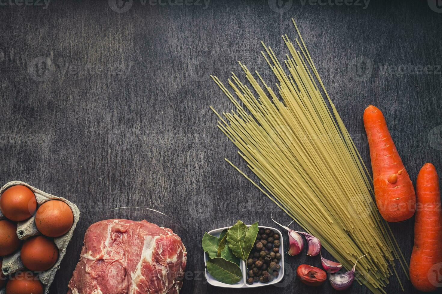 Raw meat beef slices on a wooden cutting board with spaghetti, garlic, spices, peppercorns, salt and dill for cooking pasta. Top view. photo