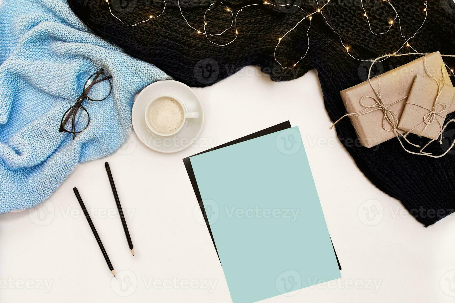 Open clean notebook for your text, pen, gift boxes, scarf and Christmas lights on white background, top view. photo