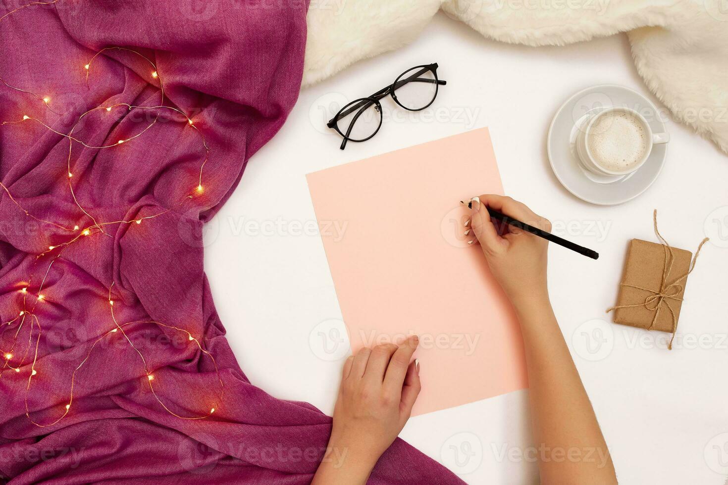 Top view of girl's hand writing in notepad placed on white surface with coffee cup and other items. Mock up photo